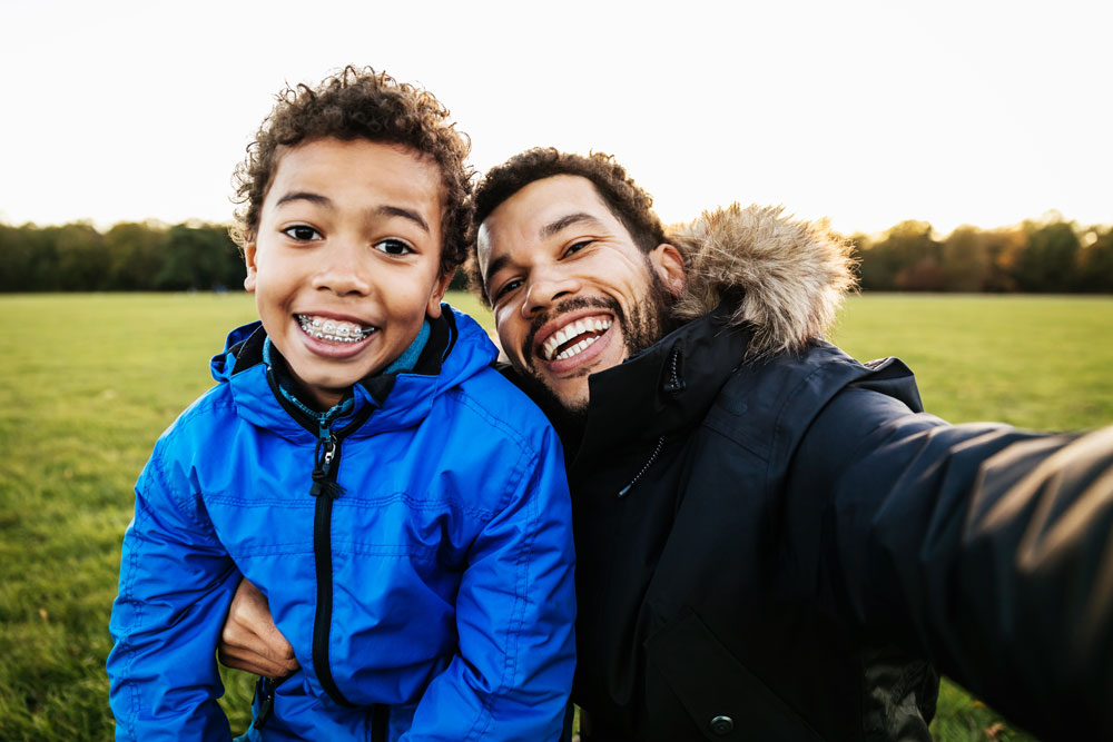 Father and son smiling while taking a self portrait, the son is showing off his braces.