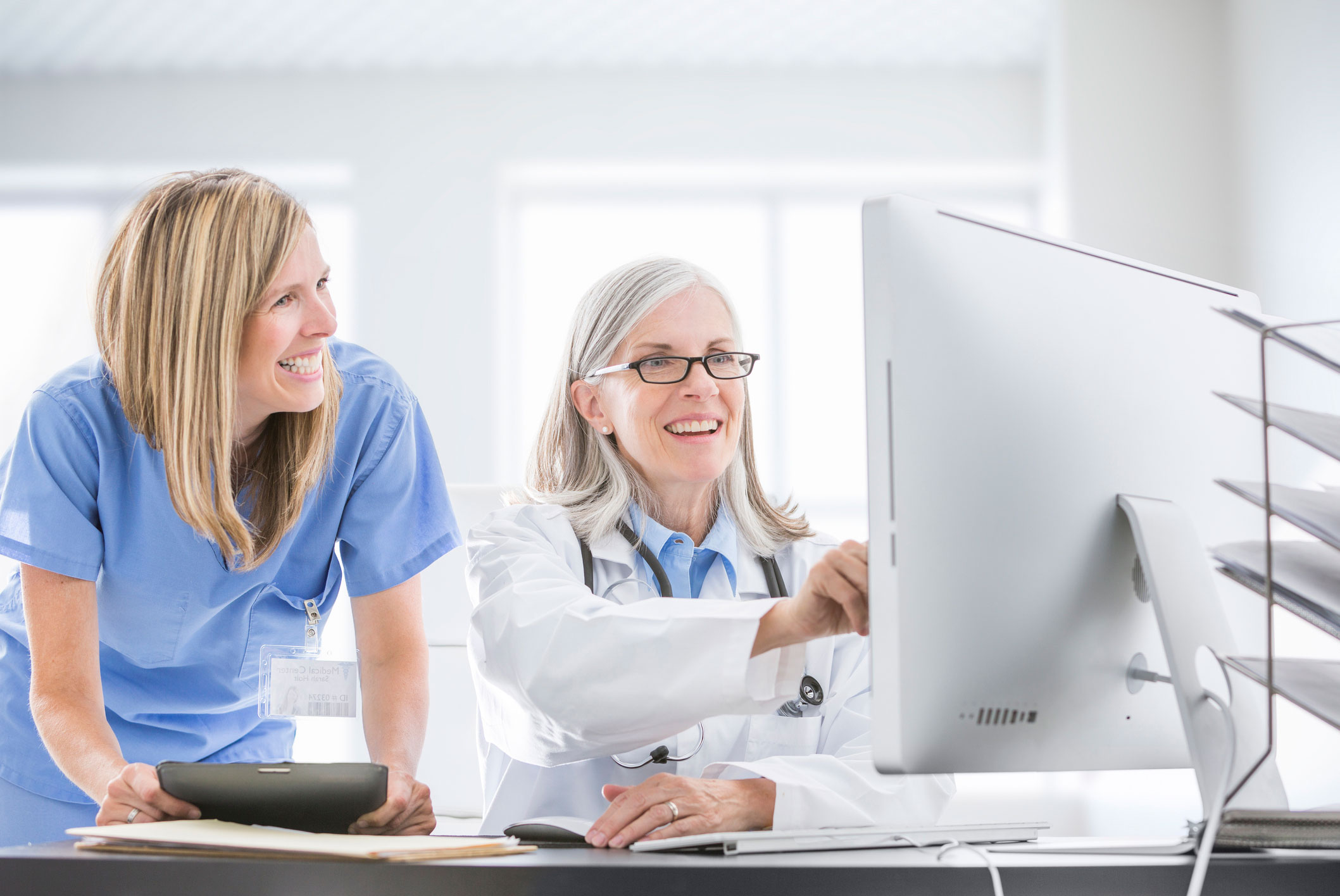 Two female medical professionals happily working together at a computer.